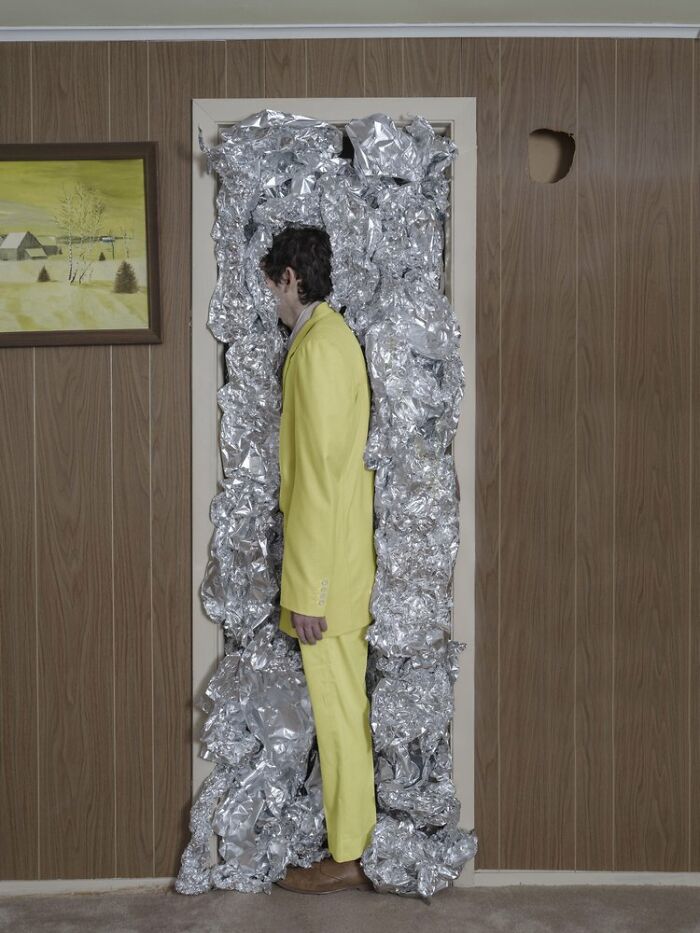 A surreal photograph by Ben Zank showing a solitary figure in a yellow suit standing in a doorway filled with foil.