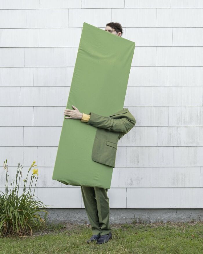 A surreal photograph of a solitary figure holding a large green rectangle against a white wall.