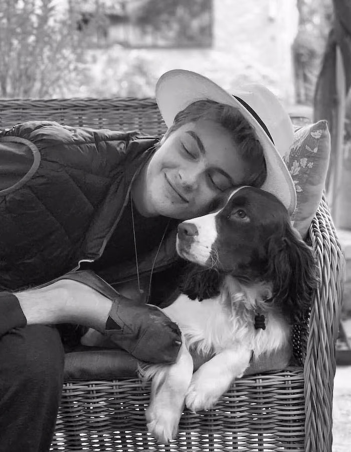 Young man in a white hat cuddling with a dog on a wicker chair, smiling peacefully. Young man in a white hat cuddling with a dog on a wicker chair, smiling peacefully.