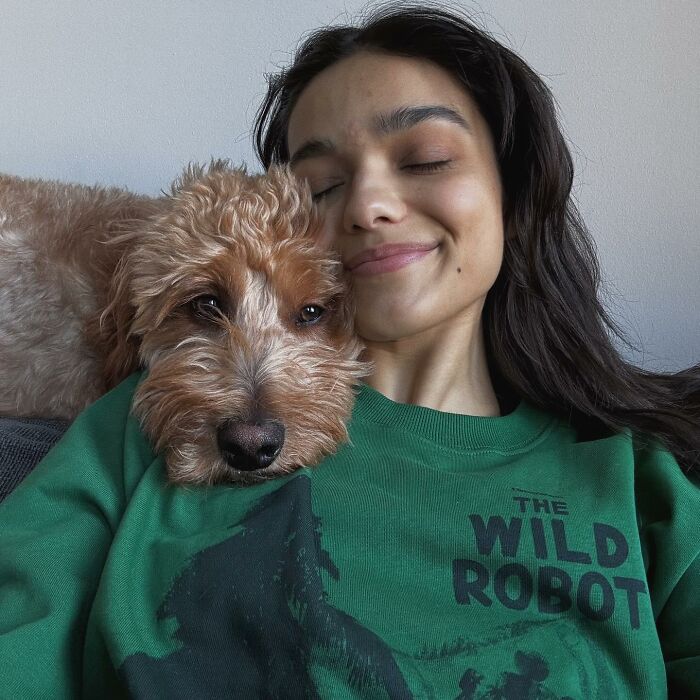 Woman smiling with eyes closed, wearing a green sweatshirt, cuddling a dog.