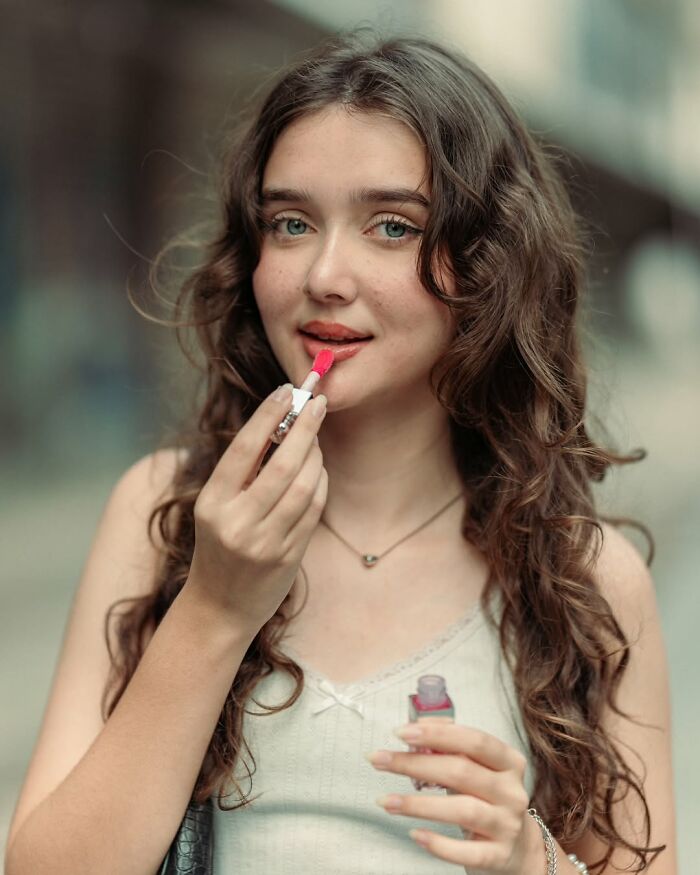 Young woman applying lipstick, captured in a stunning portrait by an Indian photographer.