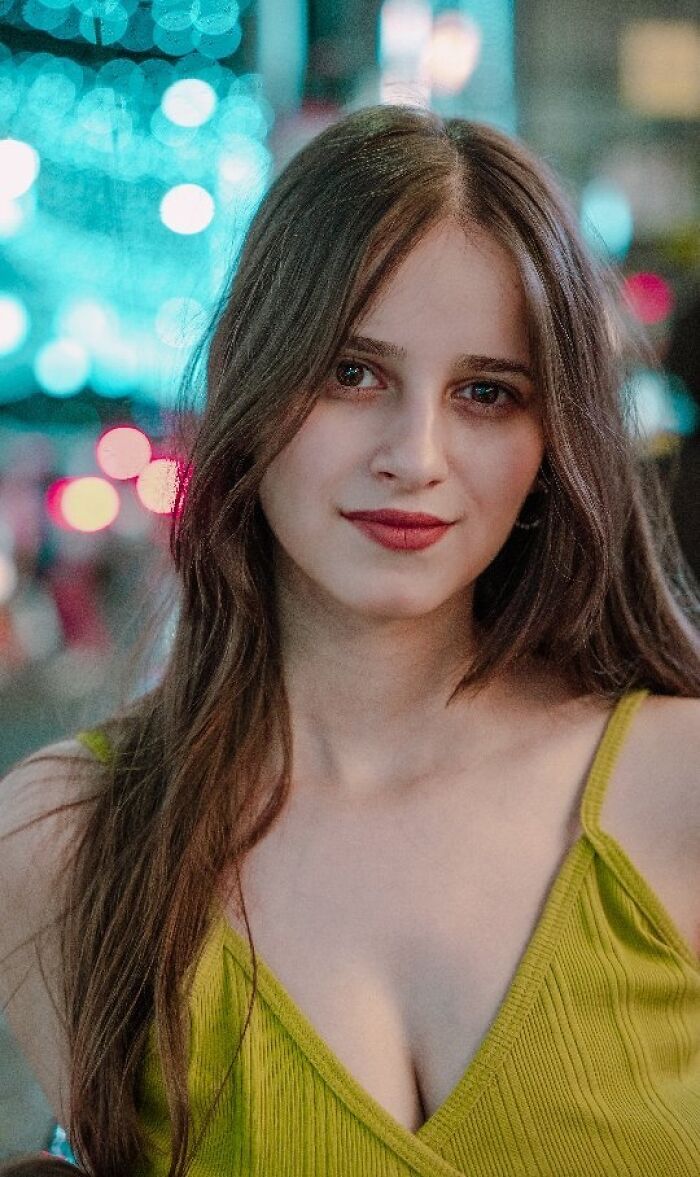 Portrait of a woman with long hair and a yellow top against a blurred city lights background, captured by an Indian photographer.