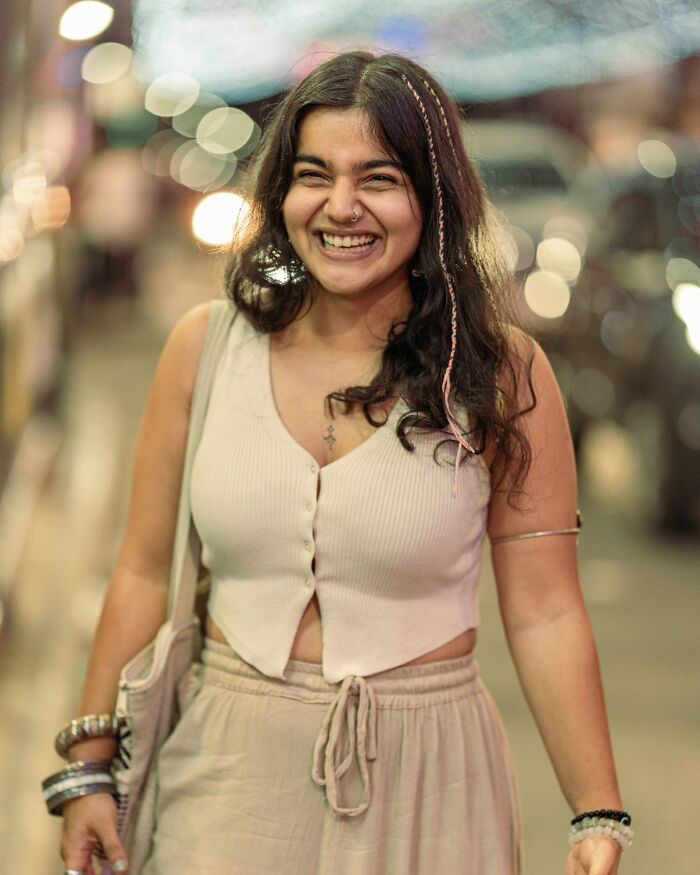 Smiling woman posing for an Indian photographer, showcasing the beauty of strangers with a city bokeh background.
