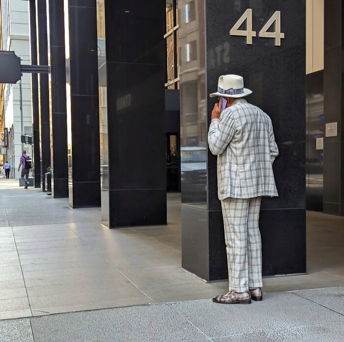 Man in plaid suit and fedora on phone, standing outside building 44 in San Francisco.