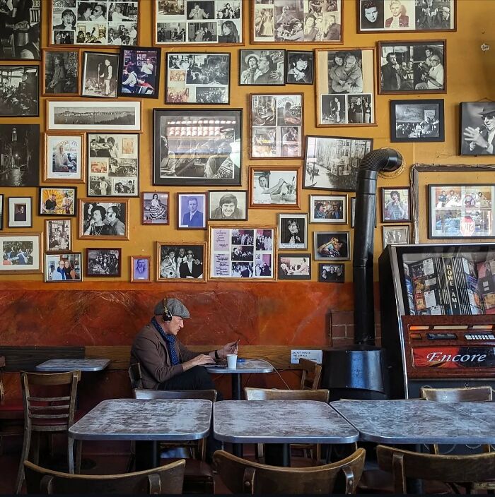 Man in a cafe, surrounded by framed photos, capturing San Francisco's essence through Sage Akaboshi’s photography.