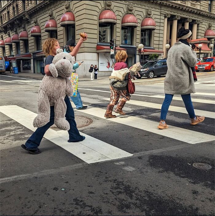 Pedestrians crossing a street in San Francisco, one holding a large stuffed animal, showcasing urban life through photography.