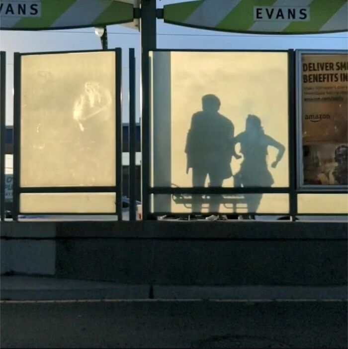 Shadows of two people on a misty glass panel at a San Francisco bus stop.