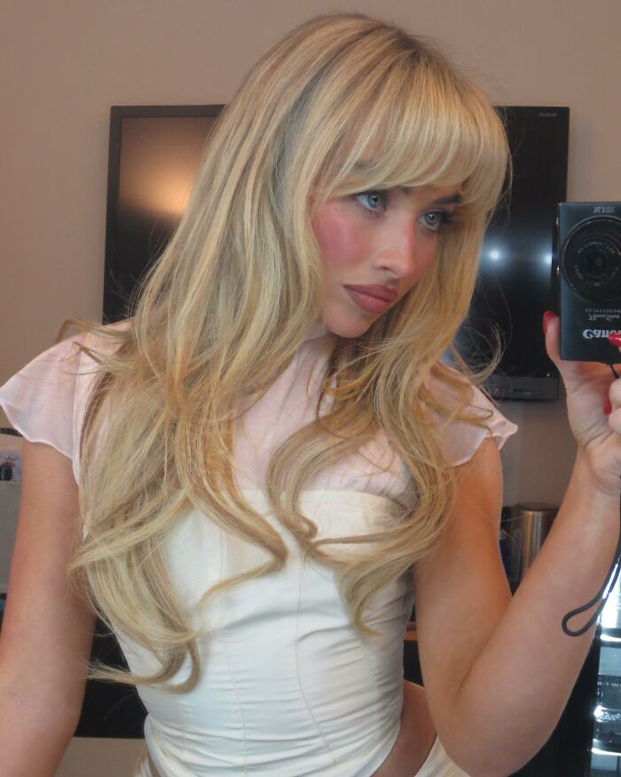 Woman taking a selfie with long blonde hair, capturing a mirror reflection in a modern setting.