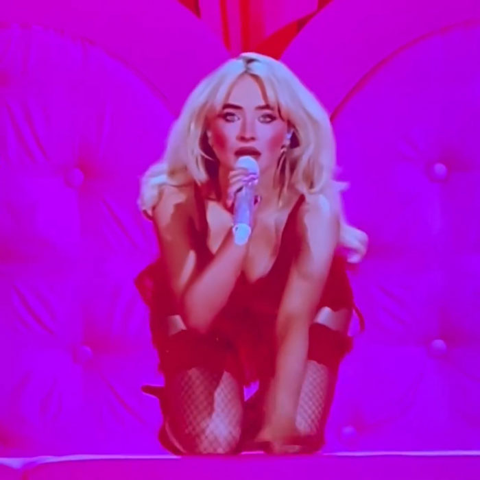 Sabrina Carpenter performs at Brit Awards in a vibrant red outfit, singing passionately into the microphone.