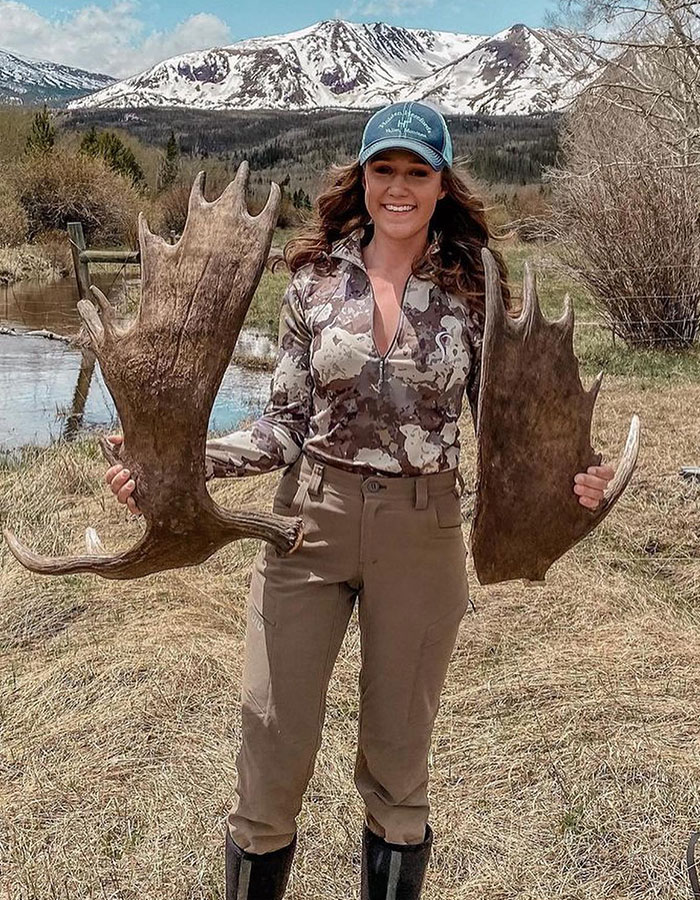 US woman outdoors holding large antlers, with snowy mountains in the background, related to wombat incident.