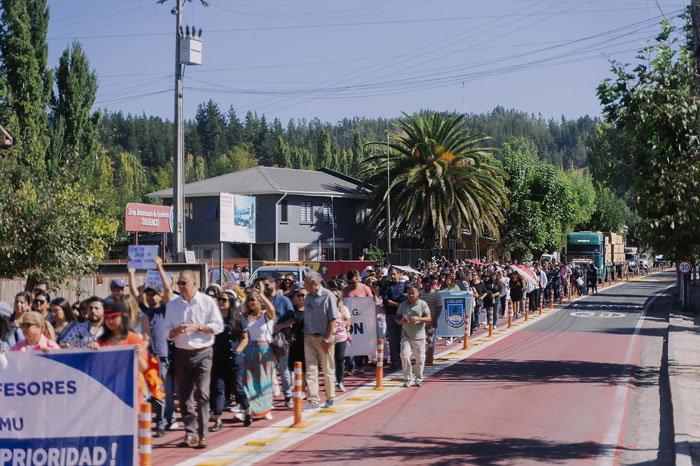 A large crowd marching down a street, holding banners and signs, with trees and buildings in the background.