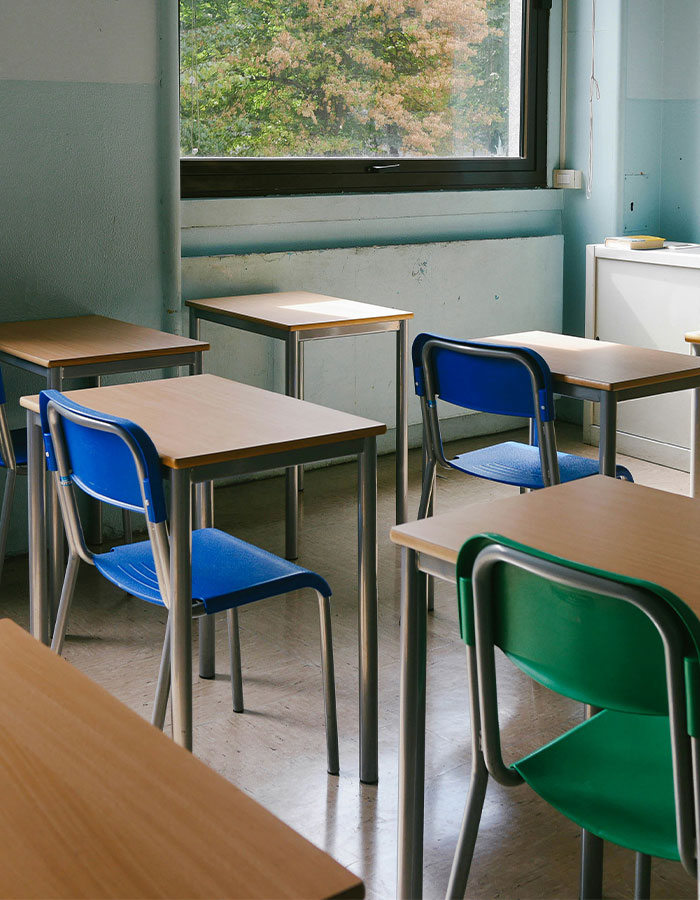 Empty classroom with blue and green chairs, natural light from a large window.