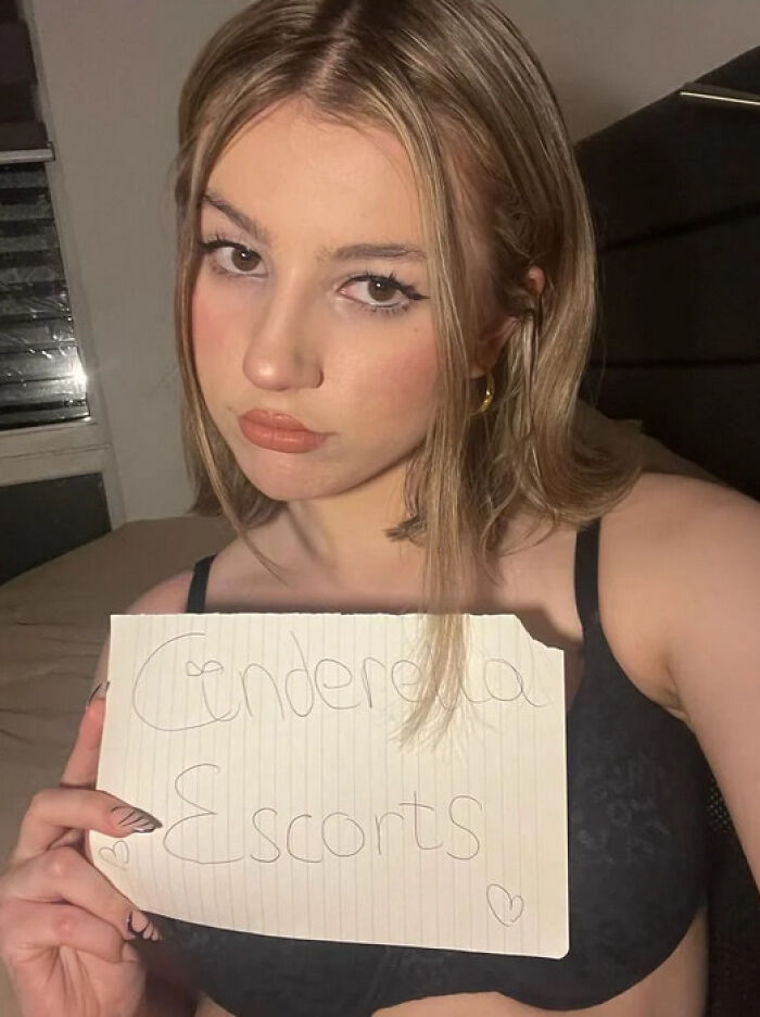 Woman holding a sign that reads "Cinderella Escorts," in a room setting. Woman holding a sign that reads "Cinderella Escorts," in a room setting.