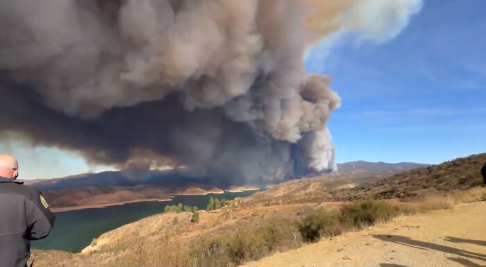 Smoke billowing from LA wildfire over hills, viewed by onlookers.
