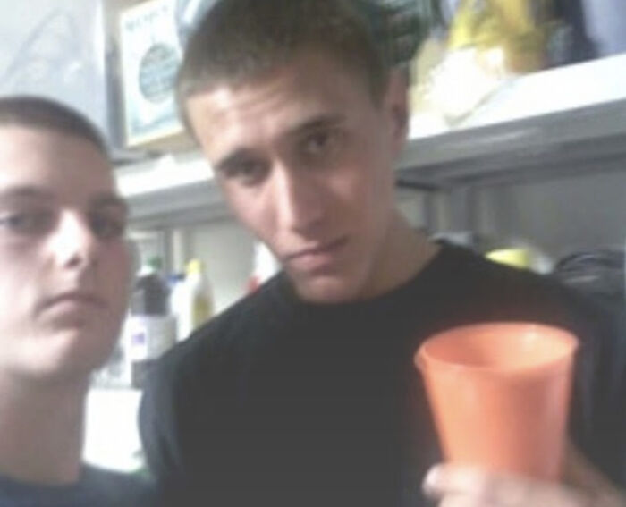 Two young men in a room, one holding an orange cup, with a seemingly normal backdrop hiding a terrifying backstory.