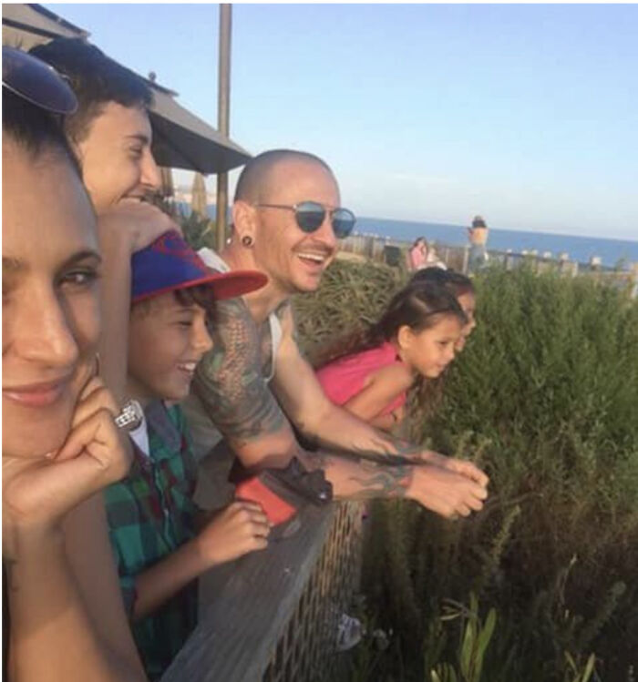 Grupo de personas sonriendo bajo el sol en un paisaje costero, sin saber la historia inquietante detrás.