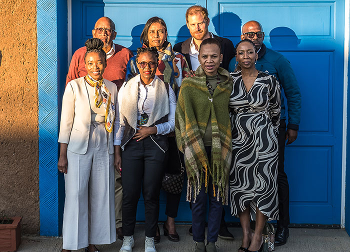 A group of people standing together in front of a blue door, related to Prince Harry's charity.