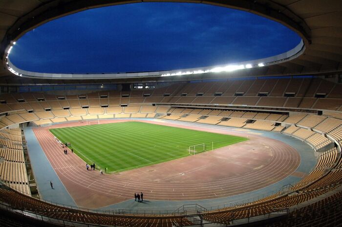 Large empty soccer stadium at dusk with bright lights and a green field, showcasing iconic cathedrals of soccer.