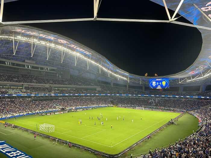 Nighttime view of a packed soccer cathedral stadium with fans watching an intense match under stadium lights.