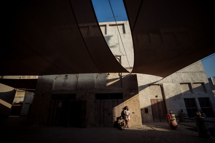 Couple posing for engagement photos in a rustic building with dramatic shadows and sunlight.