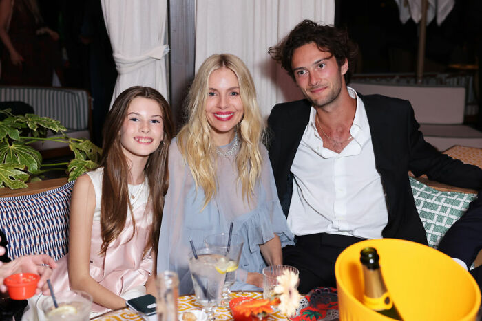 Three people sitting together at a stylish event, with Sienna Miller in the center, smiling and enjoying the evening. Three people sitting together at a stylish event, with Sienna Miller in the center, smiling and enjoying the evening.