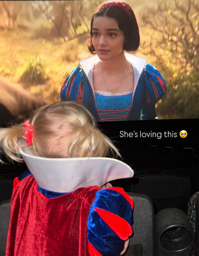 Child in a Snow White costume watching Disney's new Snow White film in a theater.