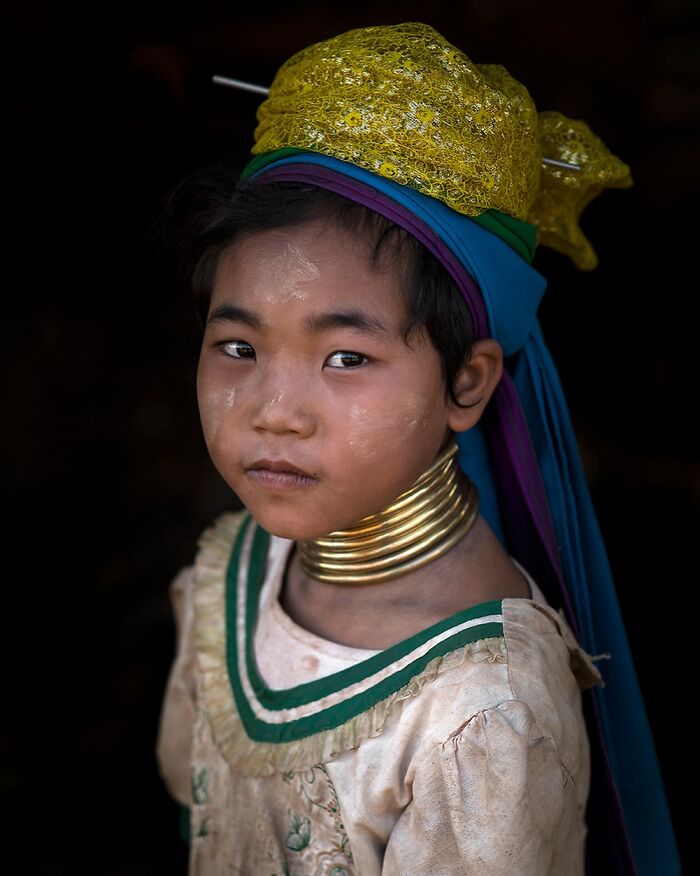A young girl in traditional cultural attire with neck rings and face paint, showcasing global cultural beauty.