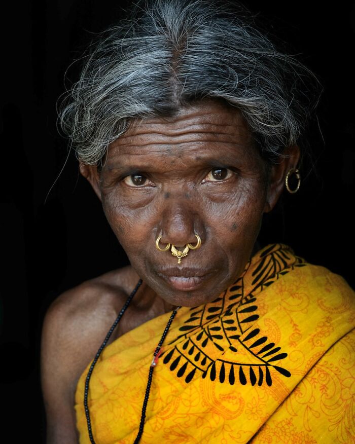 Elderly woman in vibrant yellow sari, adorned with nose rings, capturing cultural beauty and diversity.