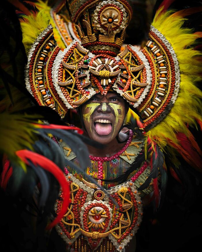 Person adorned in vibrant, intricate cultural attire with a colorful feathered headdress, embodying the beauty of cultures.