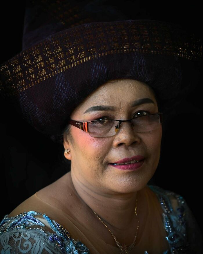 Woman in traditional attire with a dark headdress and glasses, showcasing cultural beauty.