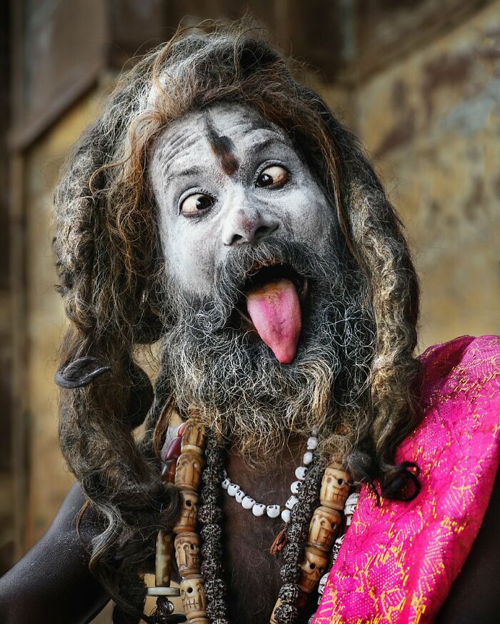 A person with face paint and beads showcases cultural beauty, sticking out their tongue in a vibrant display.