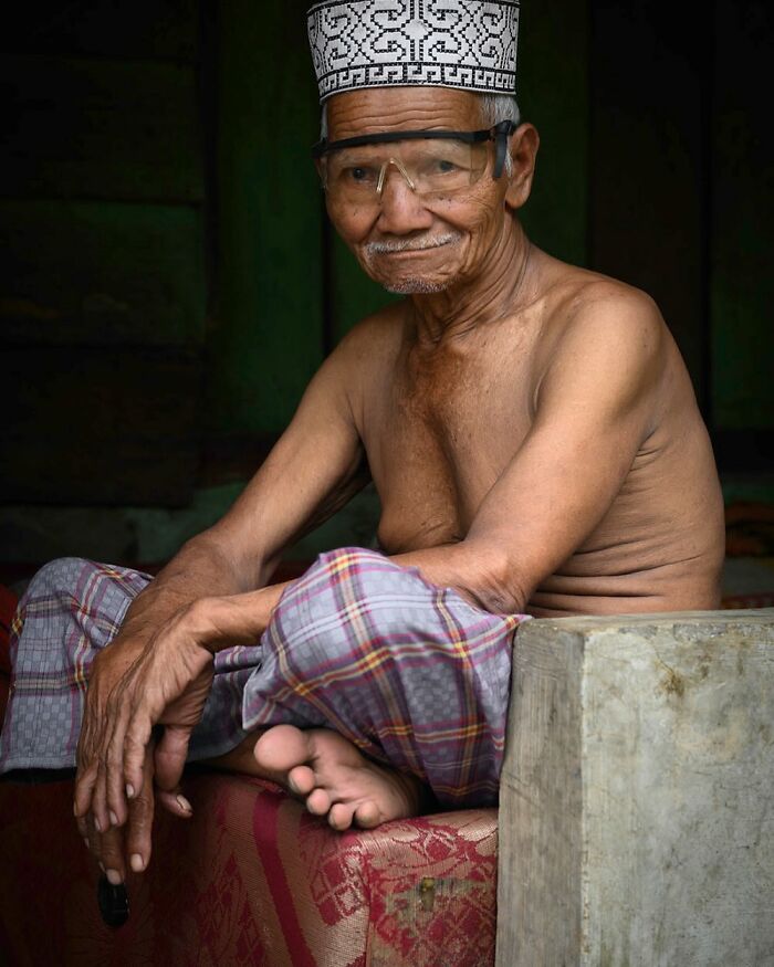 Elderly man in traditional attire and glasses, sitting comfortably, capturing cultural beauty.