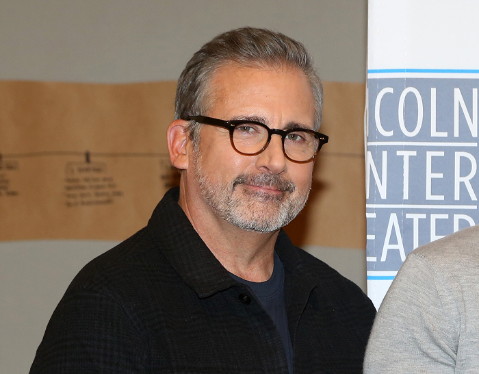 Man with glasses smiling, standing in front of a theater sign, representing celebrities attractive in person.