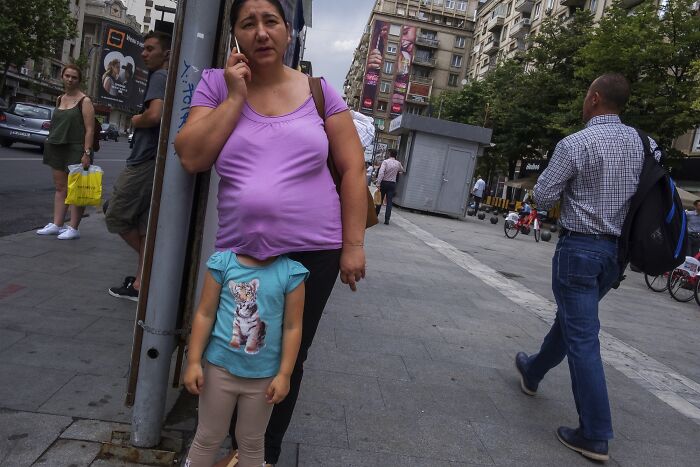 Woman on phone, creating a humorous illusion with child wearing a cat shirt in a perfectly timed street photo.