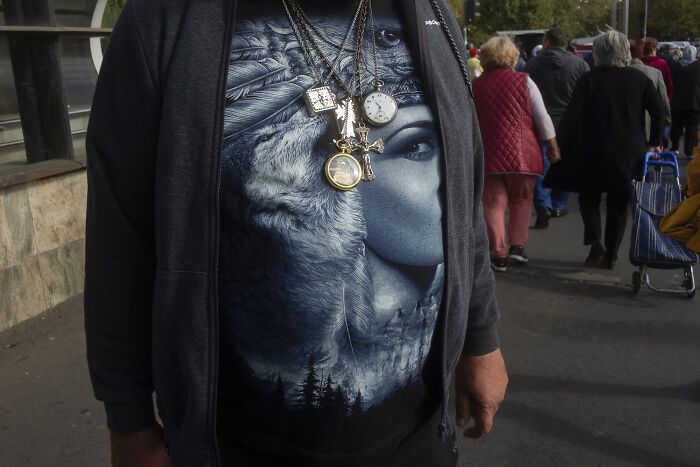 Person with wolf face T-shirt and layered necklaces in a busy street, capturing an everyday comedy moment.