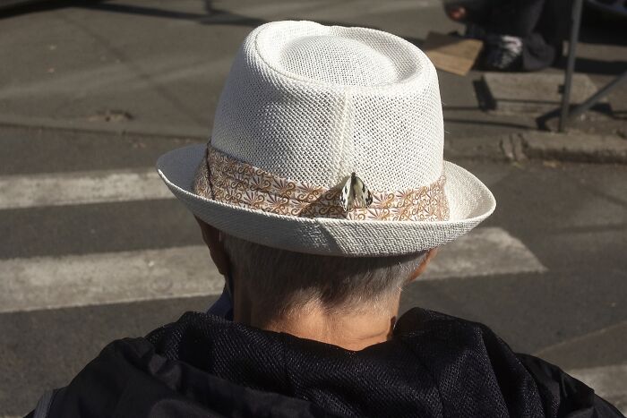 A butterfly perched perfectly on a white hat, creating a humorous street photo moment.