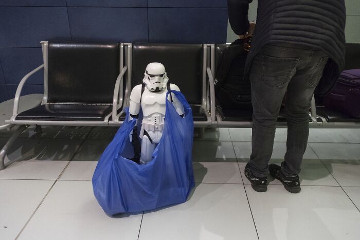 Stormtrooper in blue bag on airport seat next to person, showcasing street photography humor by Cosmin Gârleșteanu.