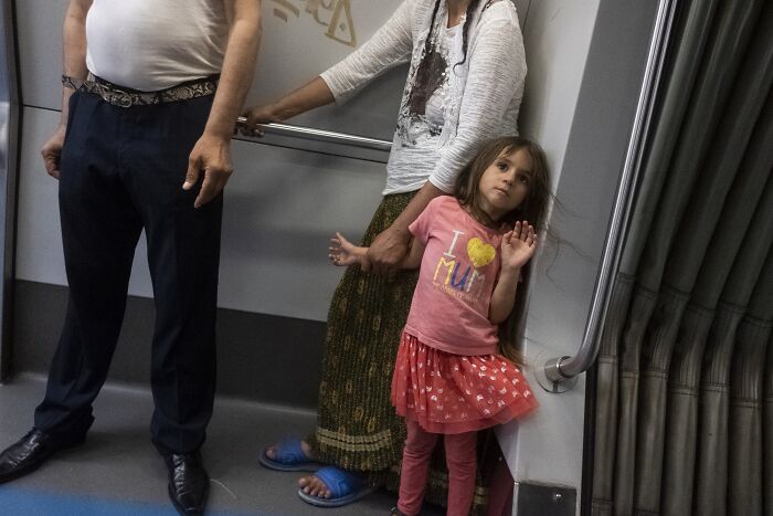 Child posing humorously next to adults in a metro, capturing a perfectly timed street photo moment.