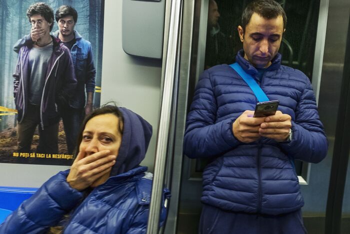A perfectly timed street photo with two people on public transport, one with a hand on their mouth, creating a humorous scene.
