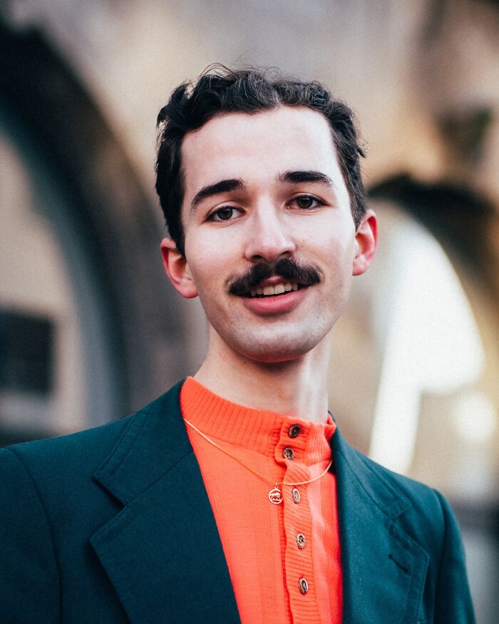 A visually striking street portrait of a young man in an orange shirt and green jacket, captured by a photographer.
