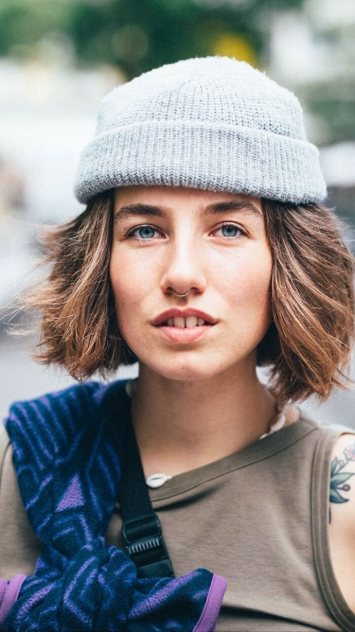 Street portrait of a visually striking woman with a gray beanie and a septum piercing, looking directly at the camera.