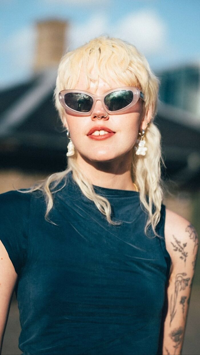 Stylish street portrait of a woman in sunglasses and a blue top, showcasing visually striking tattoos.