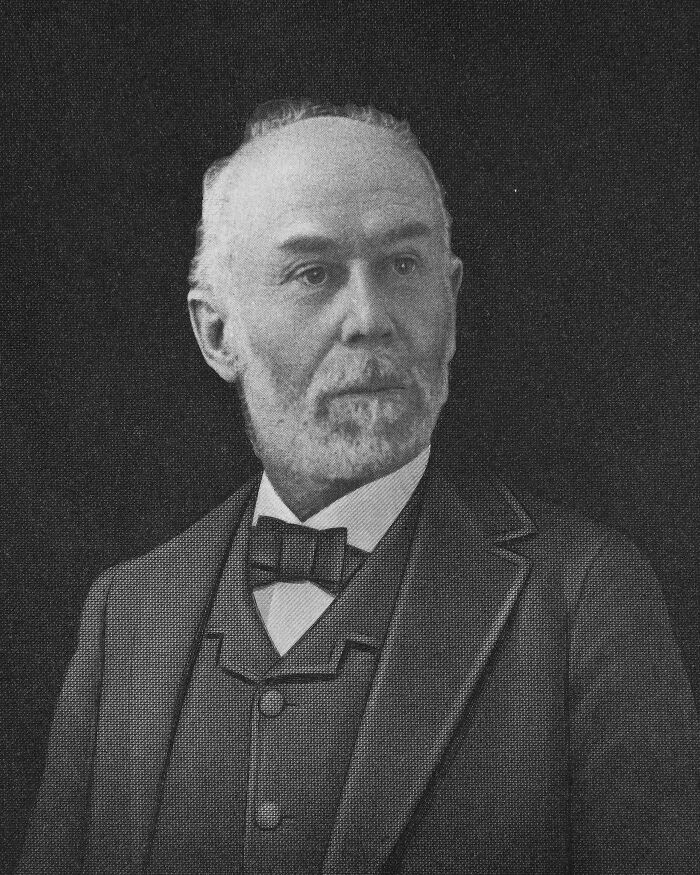 A historical inventor in a formal suit with a bow tie, portrayed in a meticulous black-and-white illustration.