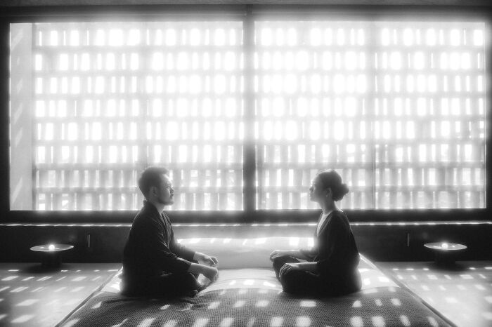Black and white engagement photo of a couple meditating in a serene, light-filled room.