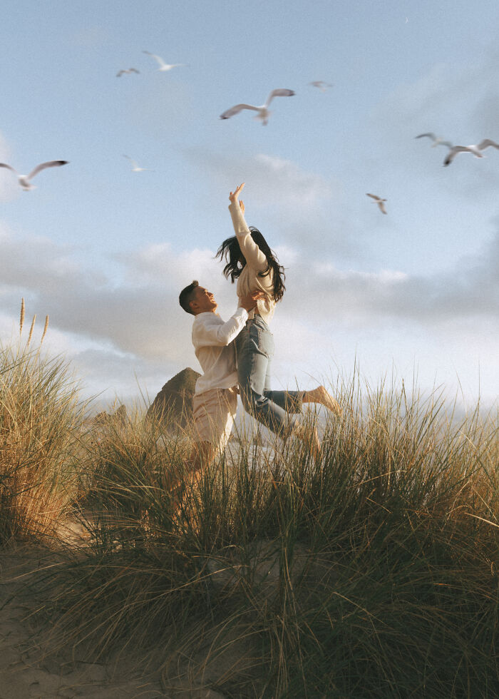 Couple in a joyful embrace at the beach, surrounded by seagulls, symbolizing top engagement photos 2025 trends.