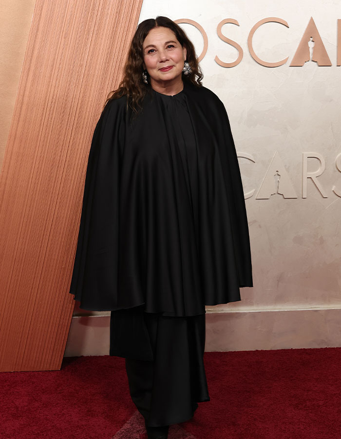 Individual in a black cape dress on the Oscars 2025 red carpet, embodying a fashionably challenged look.