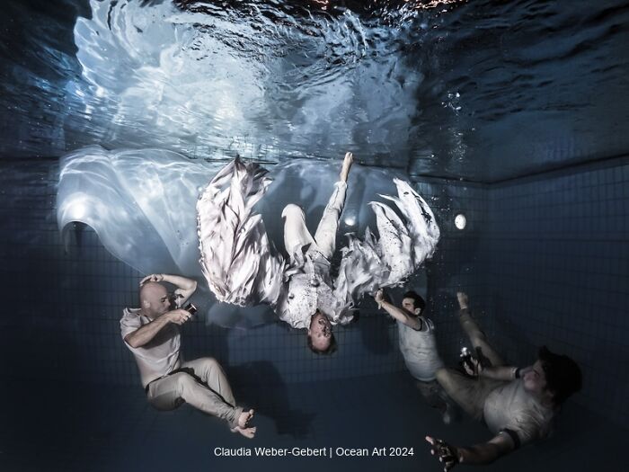 Underwater photo of three people in a pool, one inverted with flowing fabric, showcasing stunning ocean art photography.