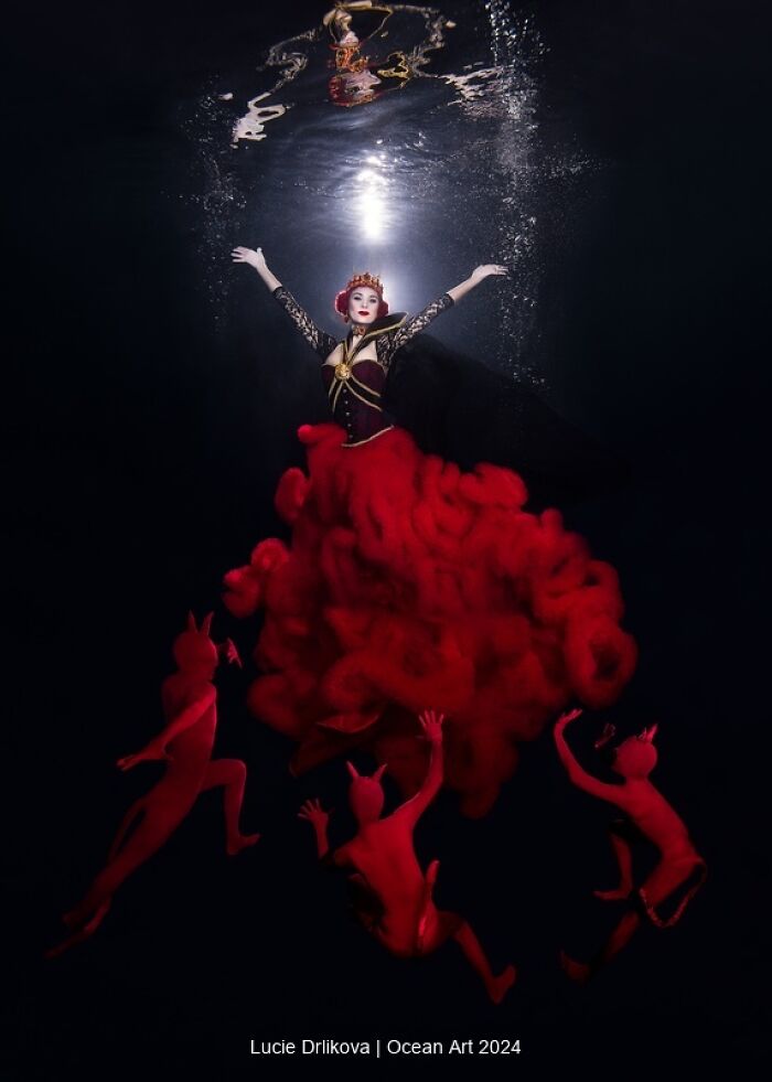 Underwater scene with a woman in red surrounded by figures, capturing a winning 2024 Ocean Art photo.