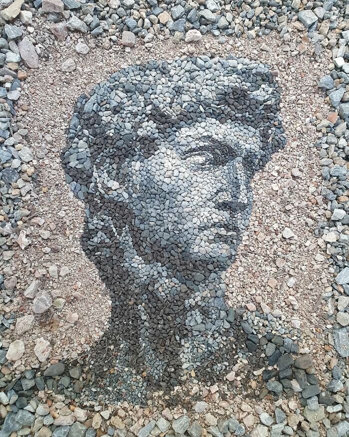 Intricate stone mosaic portrait on ground, showcasing artistic use of pebbles and stones for temporary art.