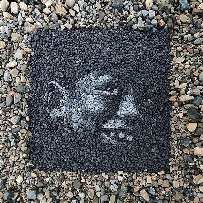 Intricate stone and pebble mosaic of a smiling face created by a British artist on a textured ground.